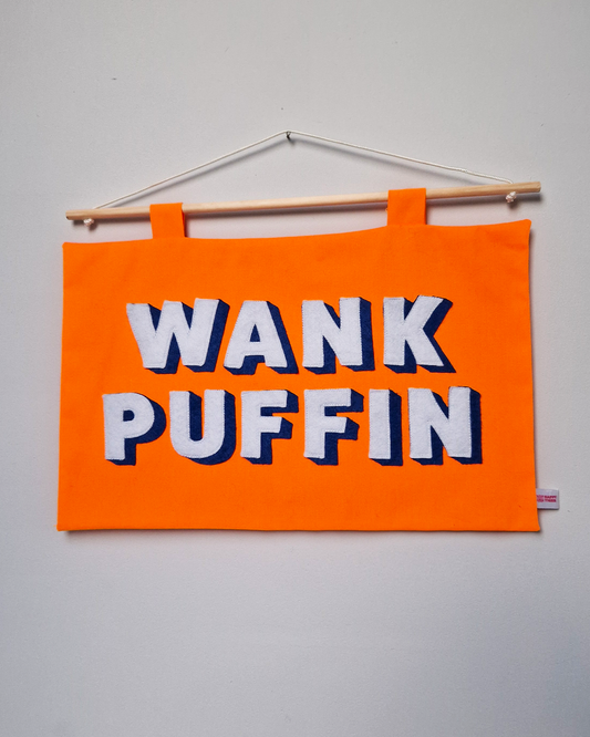 Orange Wank Puffin wall hanging banner by The Happy Tiger with bold lettering in white and blue hung on a grey wall